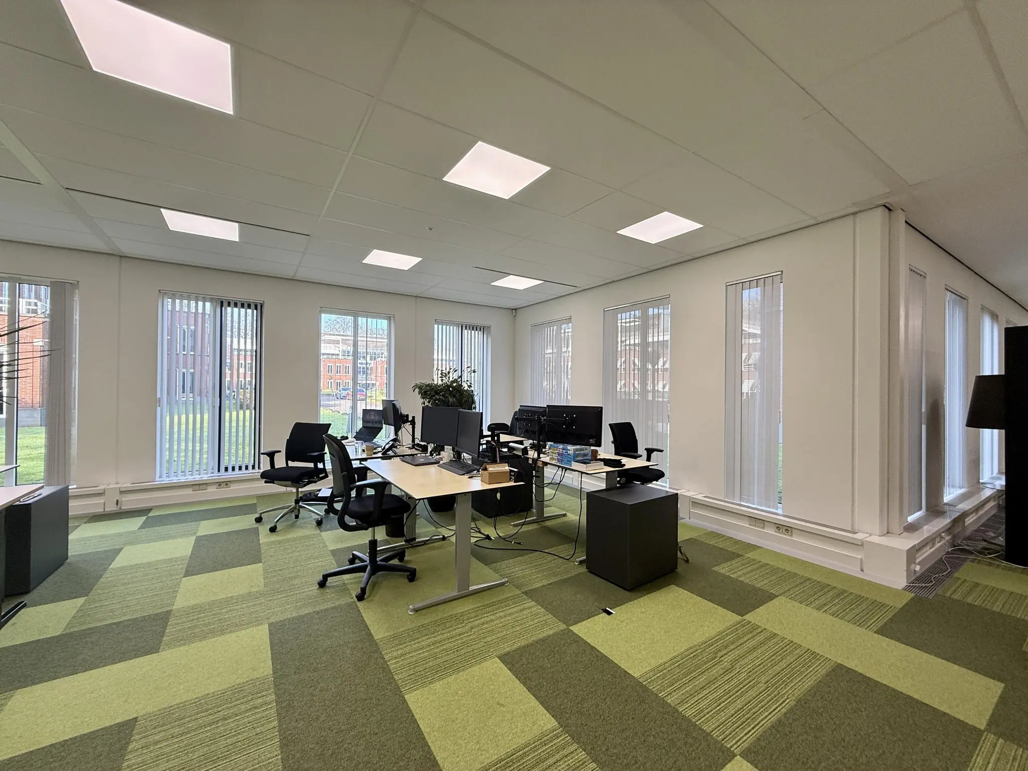 Modern kantoor met meerdere bureaus en computers aan de Arnhemse Bovenweg, met veel raamlicht en groen tapijt.